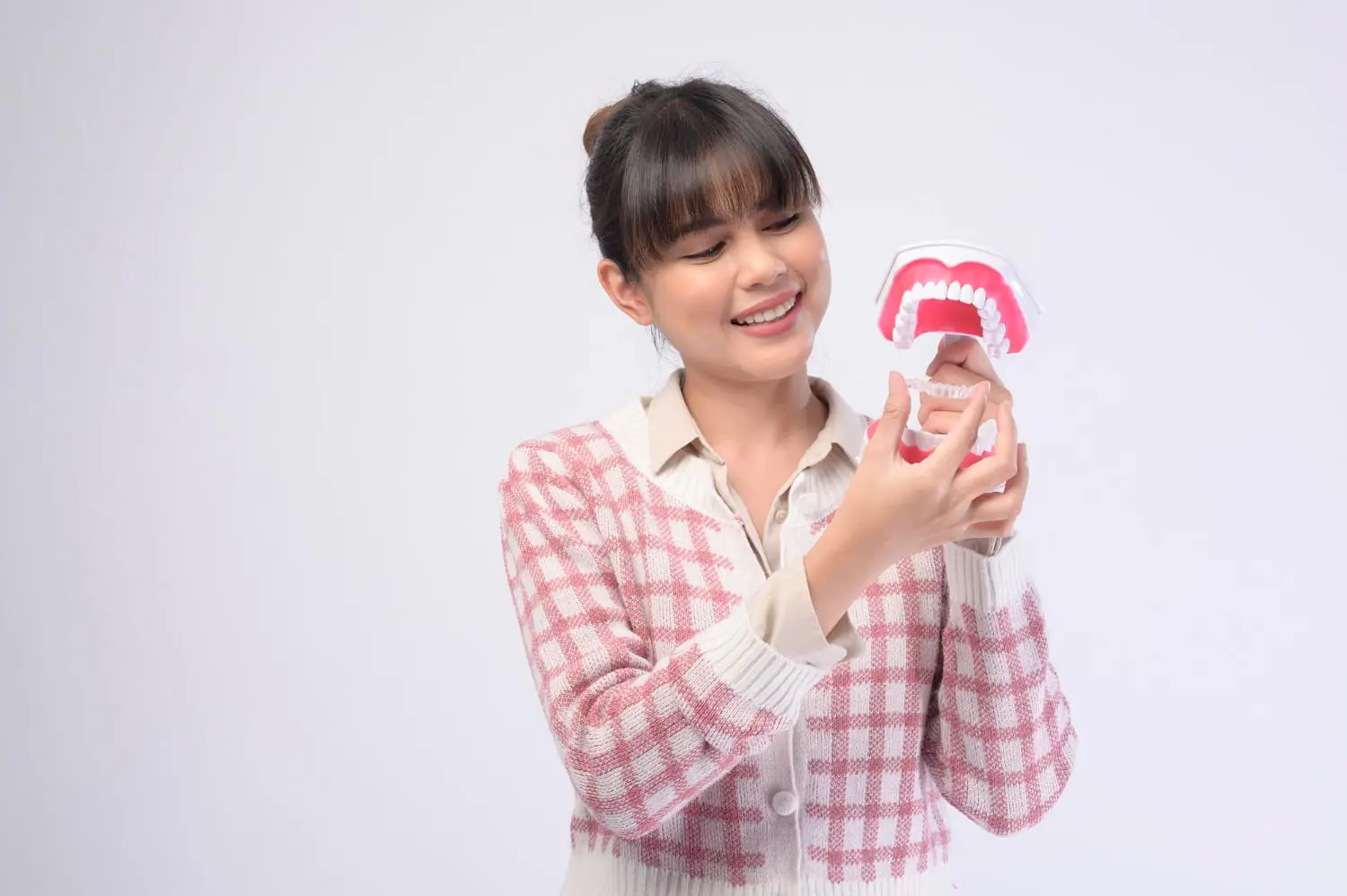 A smiling woman holds a model of teeth, possibly demonstrating Invisalign treatment offered at Chauncey Orthodontics in Henderson, NV.