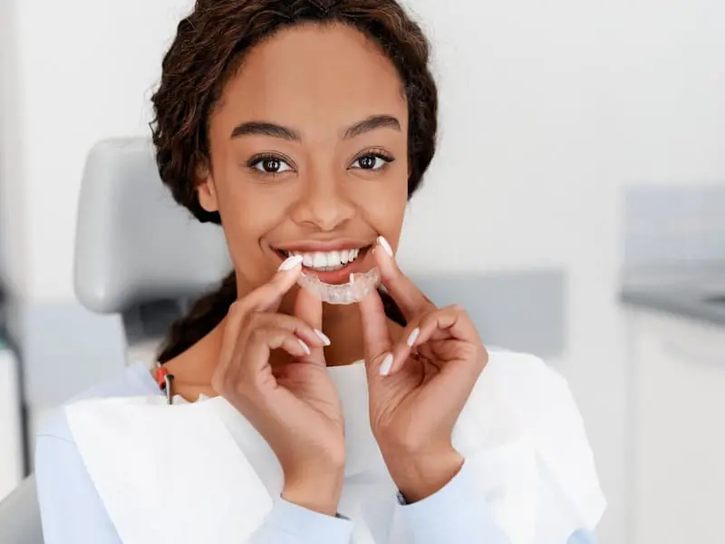 A woman, who appears to be Black, holds clear aligners, possibly Invisalign, suggesting treatment at Chauncey Orthodontics in Henderson, NV.