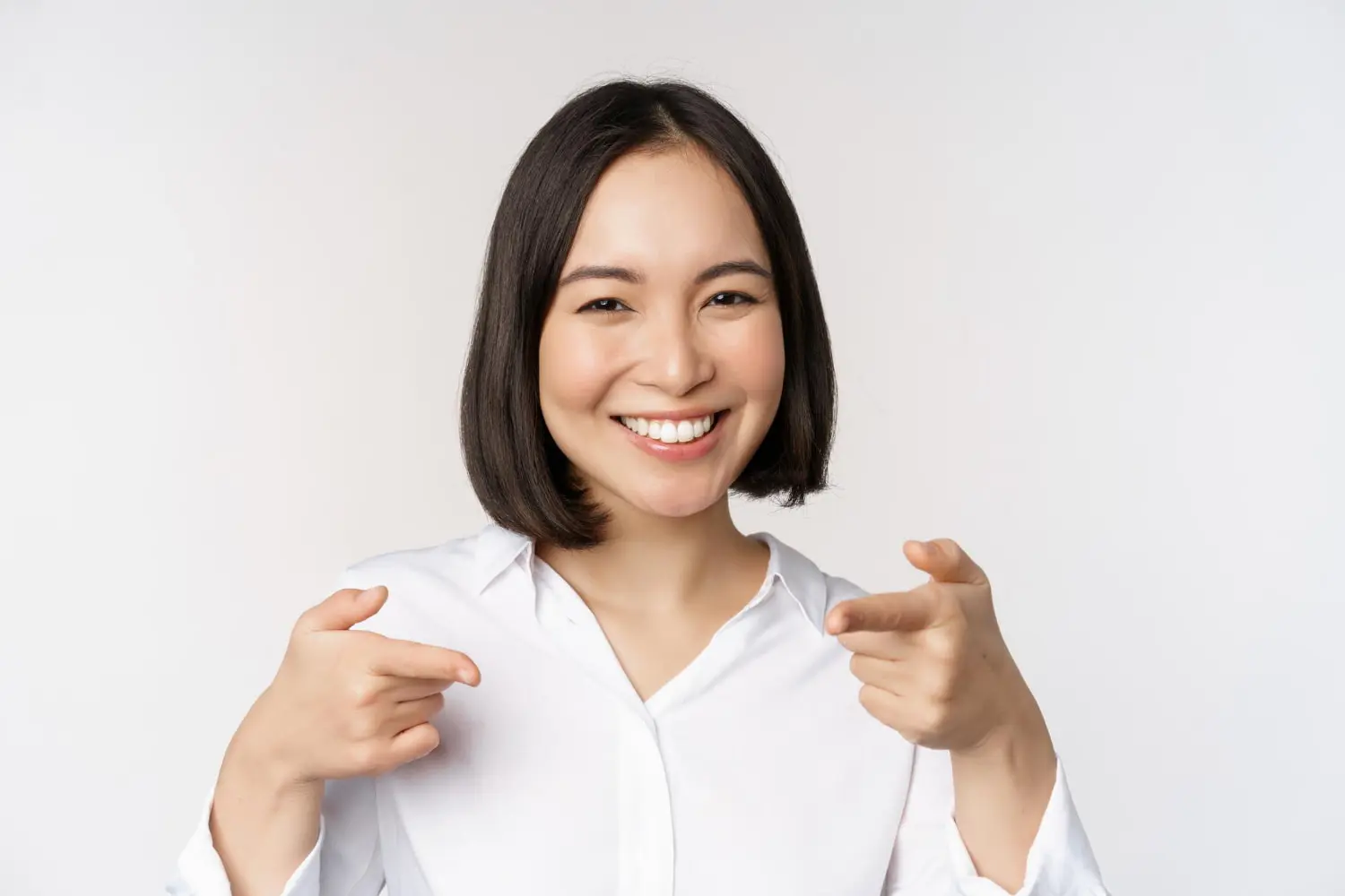 A smiling person points to their teeth. Perhaps they achieved this smile with Invisalign from Chauncey Orthodontics in Henderson, NV.