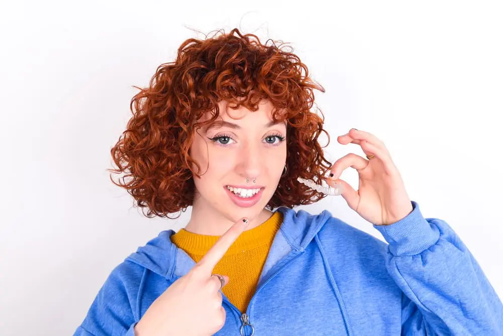 A person with curly red hair points to clear Invisalign aligners they are holding. Chauncey Orthodontics in Henderson, NV offers these.