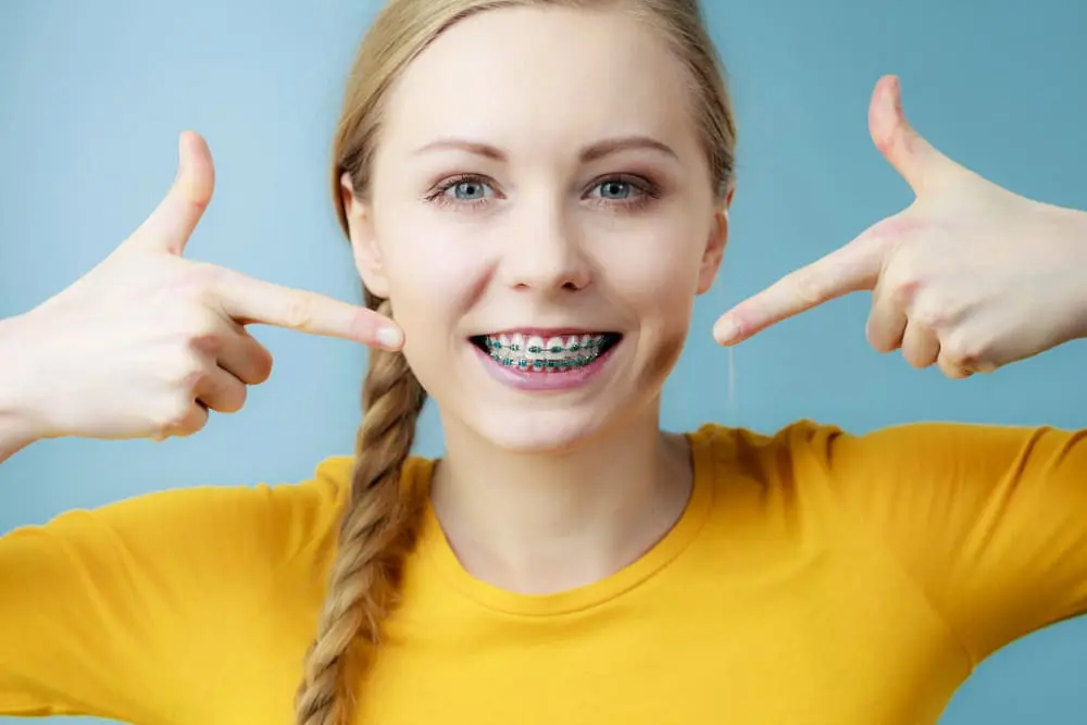 A smiling person points to their metal braces. Chauncey Orthodontics in Henderson, NV offers traditional braces and other orthodontic treatments.