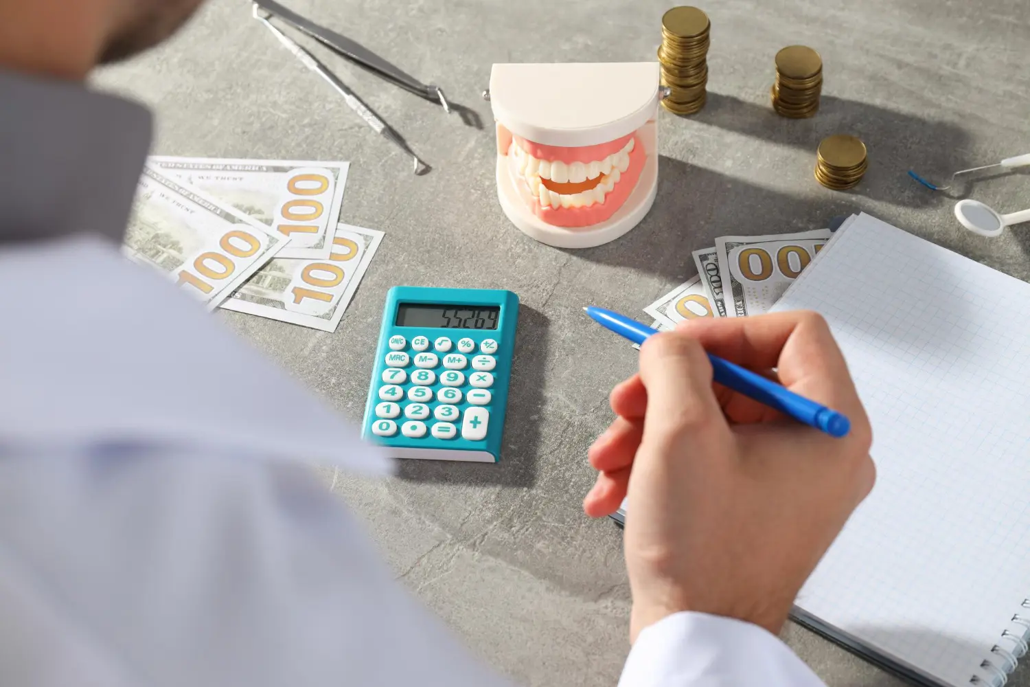 A dental professional calculates costs with a tooth model, cash, and calculator, potentially related to invisalign treatment costs in Henderson, NV.