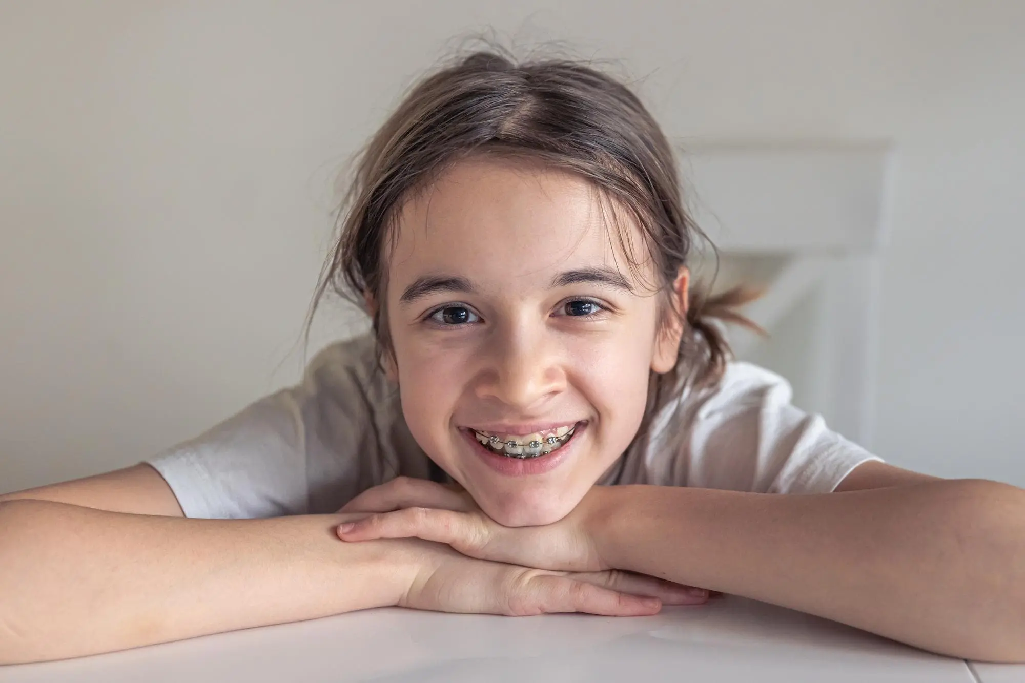 A young girl in a white shirt, smiling, proudly shows off her affordable braces from Chauncey Orthodontics in Henderson, NV.