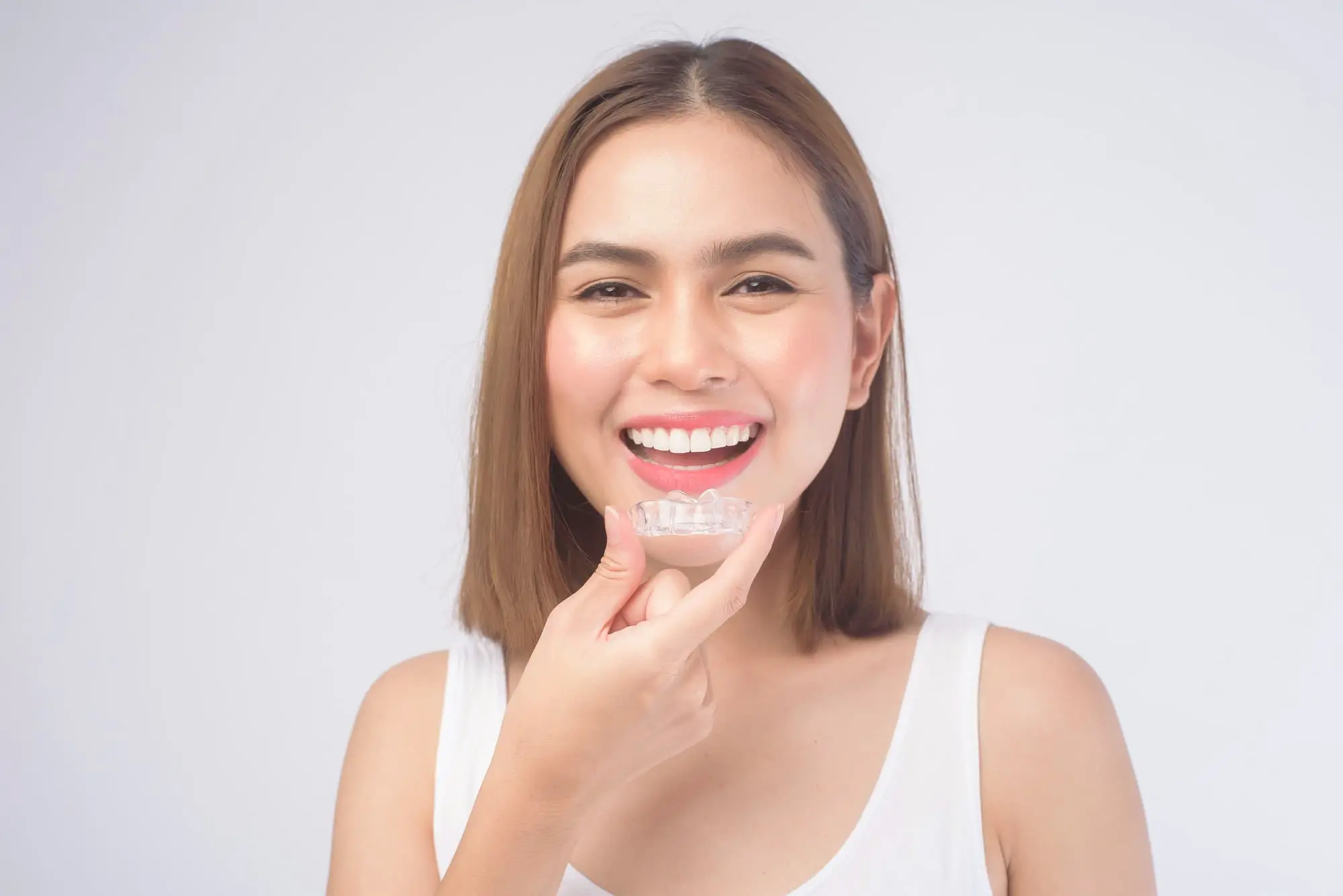 A woman smiles, while holding Invisalign® Clear Aligners available at Chauncey Orthodontics in Henderson, NV.