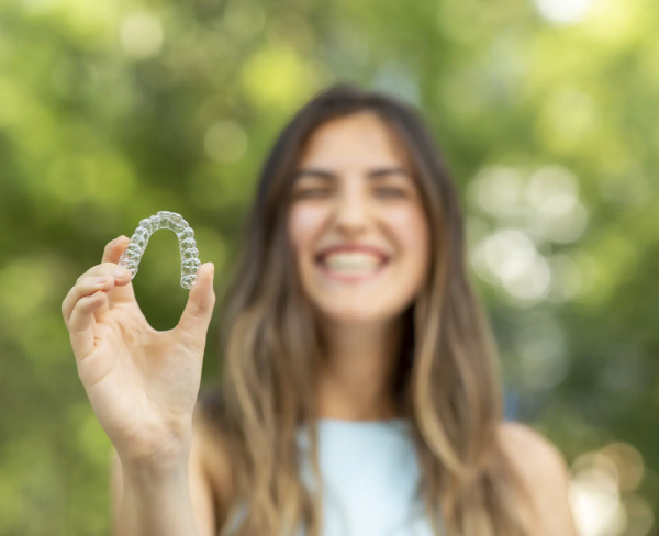 Enjoying the outdoors, a woman with a radiant smile holds a clear dental aligner. At Chauncey Orthodontics operates in Henderson NV, she explores whether treatments like Invisalign are covered by insurance, embracing confidence in every step.