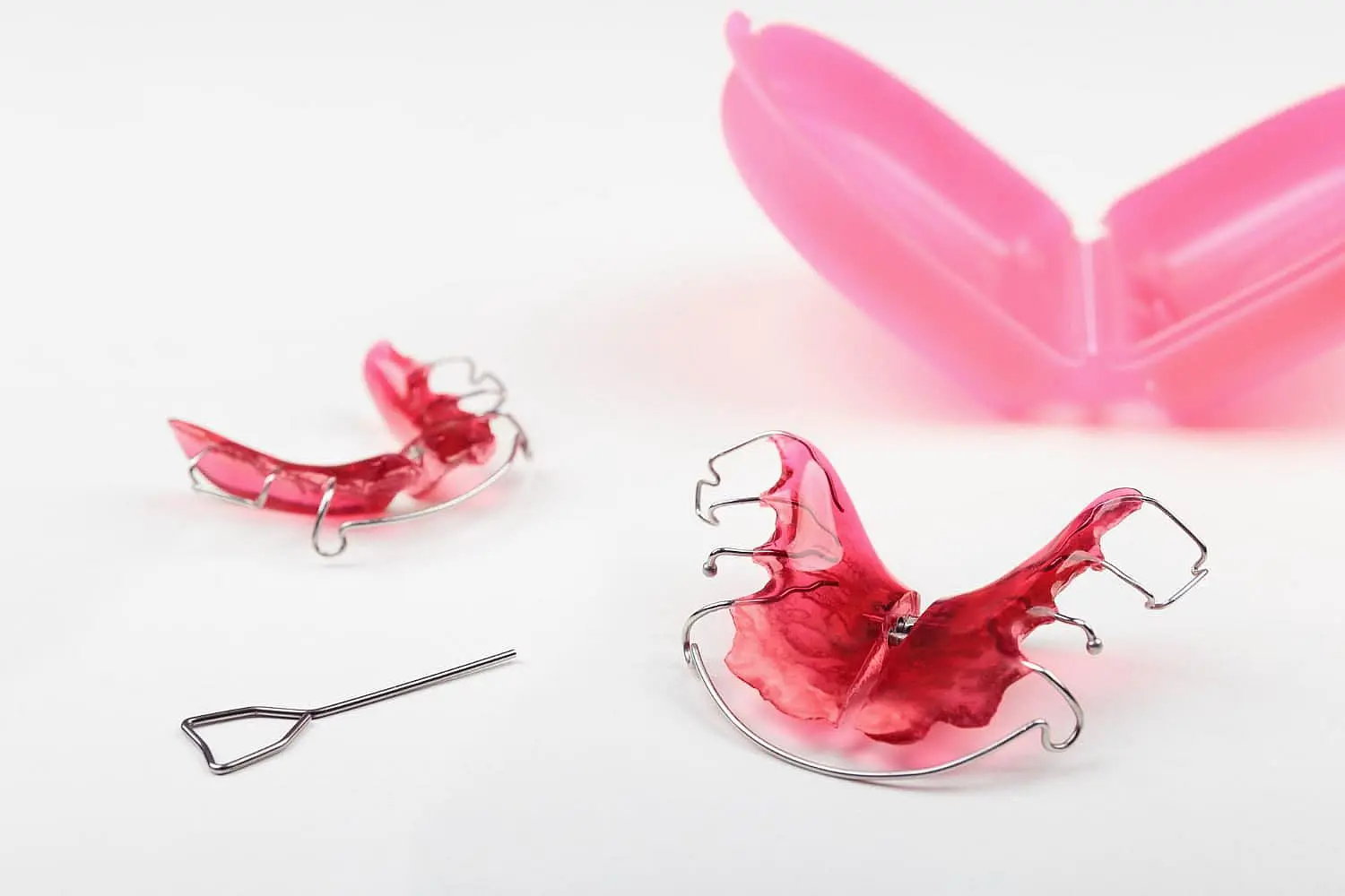 At Chauncey Orthodontics in Henderson NV, two pink orthodontic retainers, a metal adjustment key and an open pink storage case are shown on a white surface essential tools for fitting children’s functional appliances.