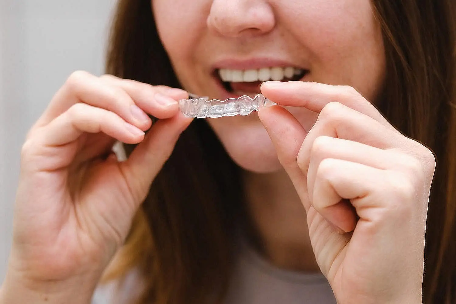 A person holding a clear dental aligner near their mouth, preparing to wear it, weighs the benefits of invisalign vs braces in achieving a perfect smile in Henderson, NV.
