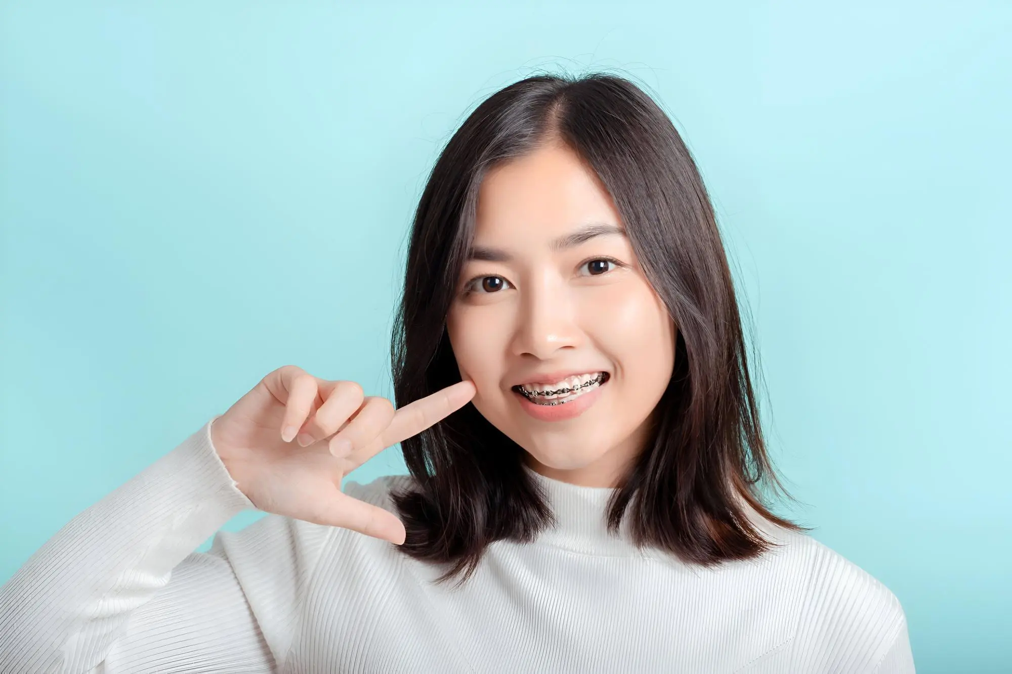 A woman with straight black hair while pointing at their teeth, show aesthetic of metal braces from Chauncey Orthodontics in Henderson, NV.