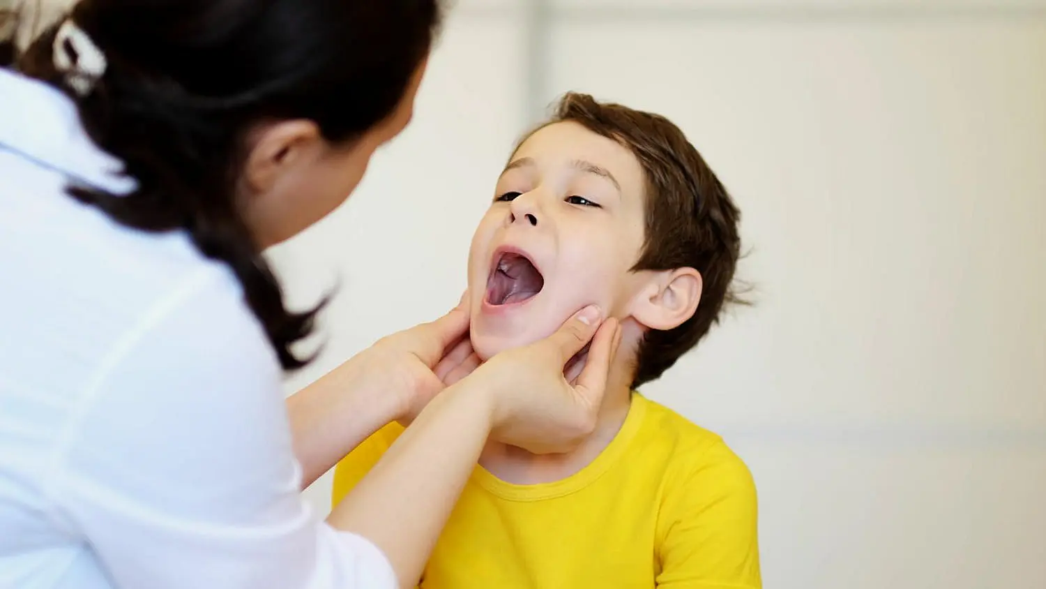 A gentle oral health check, like an initial evaluation by a children’s orthodontist at Chauncey Orthodontics in Henderson NV, is shown as an adult examines a young boy’s open mouth.