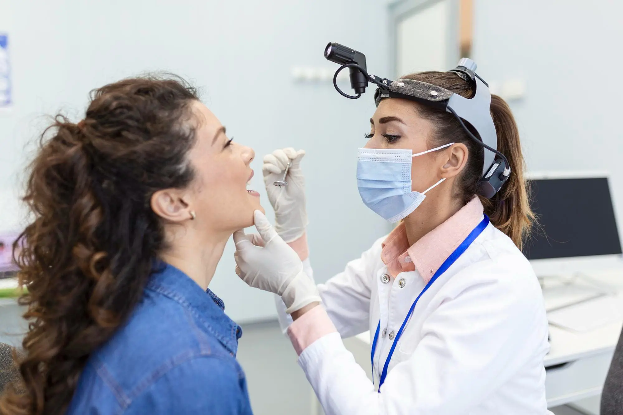 A doctor wearing a mask and headlamp examines a patient's mouth breathing issue in a medical office. The patient is sitting and opening her mouth at Chauncey Orthodontics in Henderson, NV.
