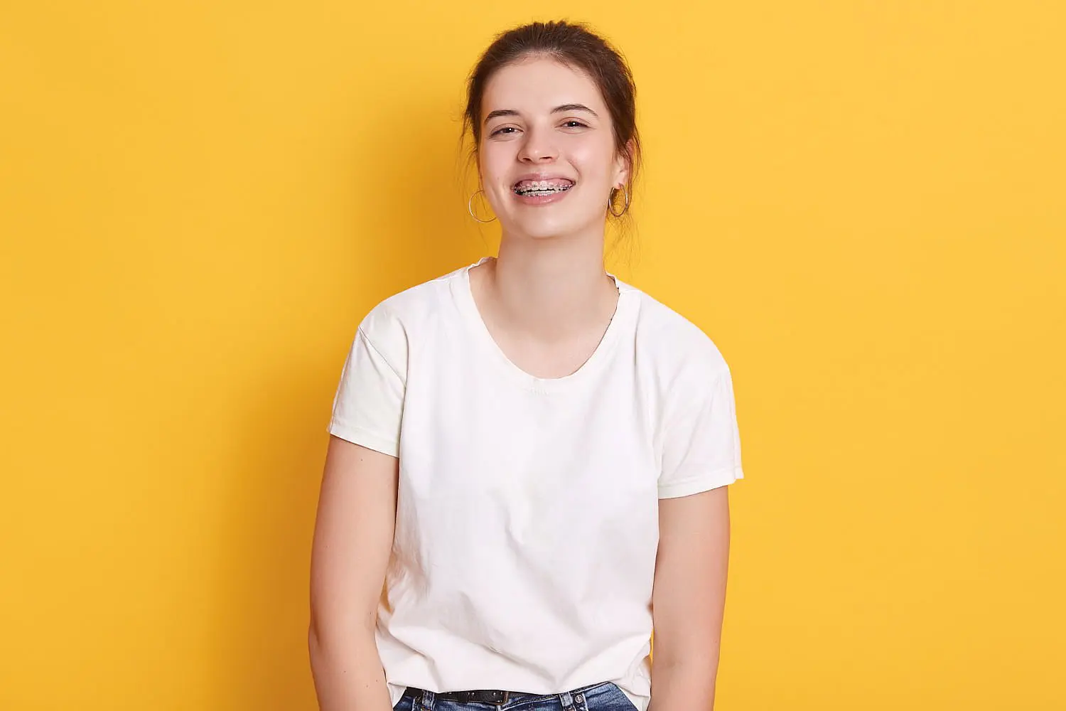 A person confidently smiles with braces and a slight underbite, posing against a bright yellow background. She have visited Chauncey Orthodontics in Henderson, NV.