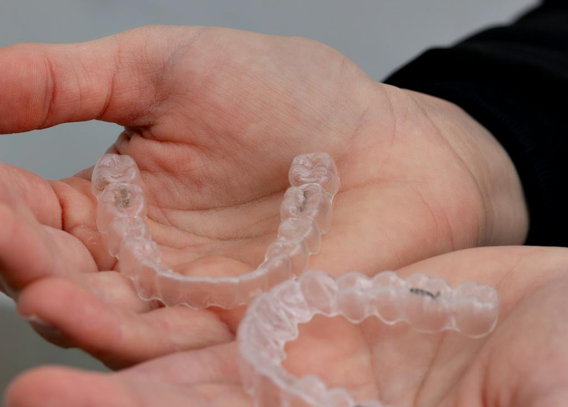 Hands holding two clear dental aligners, showcasing the benefits of a seamless smile transformation journey, potentially enhanced by an Invisalign Payment Plan in Henderson, NV.