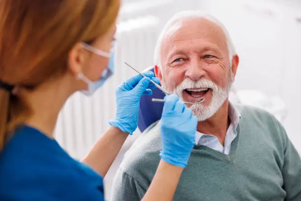 An older man sits confidently in the dental chair as a dentist in blue gloves examines his teeth for potential jaw surgery at Chauncey Orthodontics operates in Henderson, NV.
