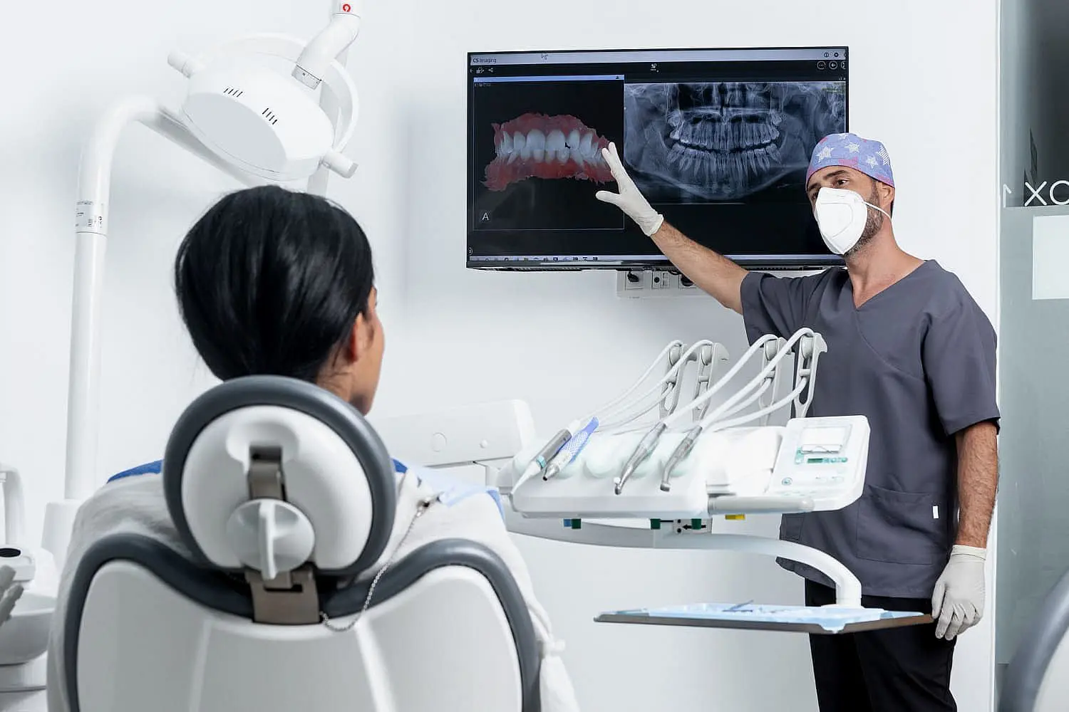 Dentist in scrubs and mask discusses dental X-rays on a monitor with a patient in the dental chair, explaining potential jaw surgery options in Henderson, NV.
