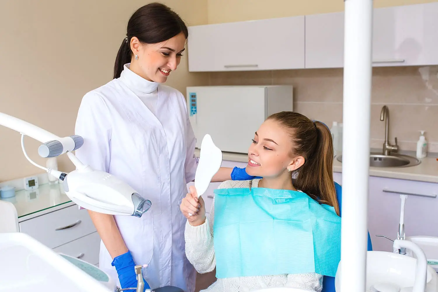 In the bright clinic, a dentist discusses the success of recent jaw surgery with a patient in a dental chair, holding a dental mirror and smiling. Chauncey Orthodontics provides similar services in Henderson, NV.