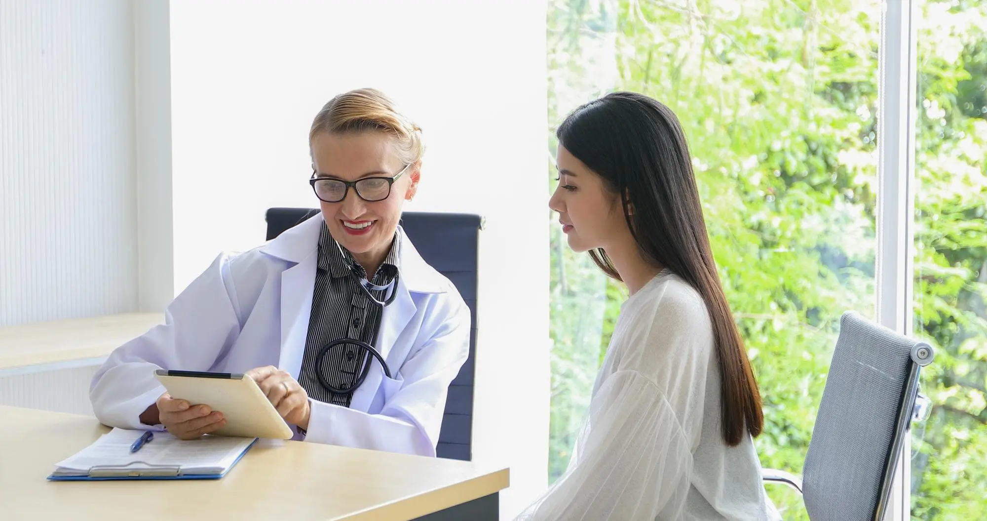 A doctor in a white coat shows a tablet explain about tongue thrust issue to a seated patient while sitting together at a desk in a brightly lit office at Chauncey Orthodontics operates in Henderson, NV.