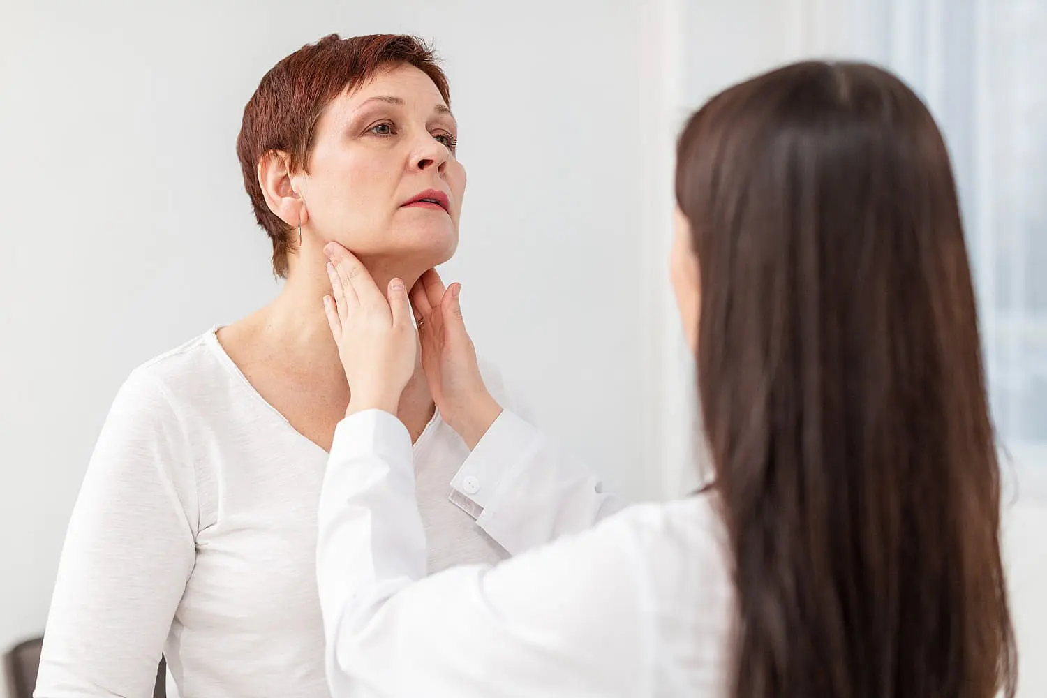 A doctor examines a woman's neck in the medical office, assessing her condition possibly related to jaw surgery in Henderson, NV.