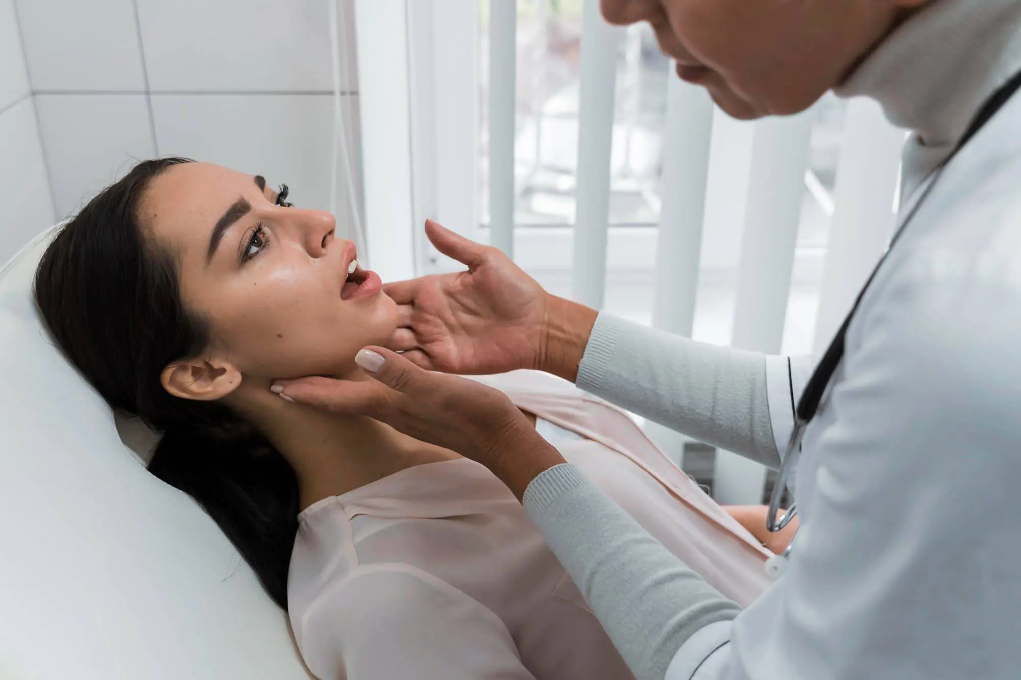 A doctor examines a woman's throat by gently holding her jaw and neck while she sits in a medical office might for plan jaw surgery at Chauncey Orthodontics operates in Henderson, NV.