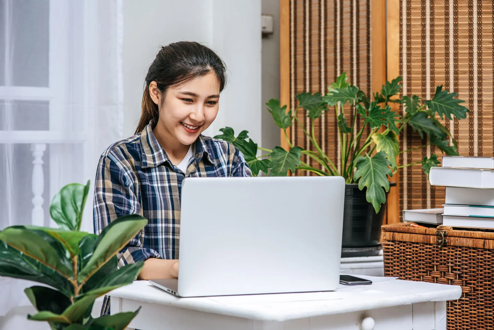 A woman sits at a desk using a laptop, smiling find affordable braces for her teeth from Chauncey Orthodontics in Henderson, NV.