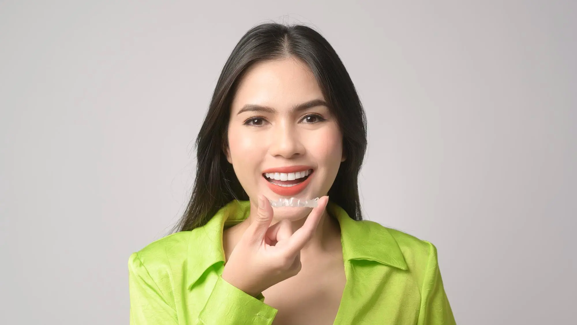 A woman smiles as she holds an affordable invisalign clear aligner at Chauncey Orthodontics operates in Henderson, NV.