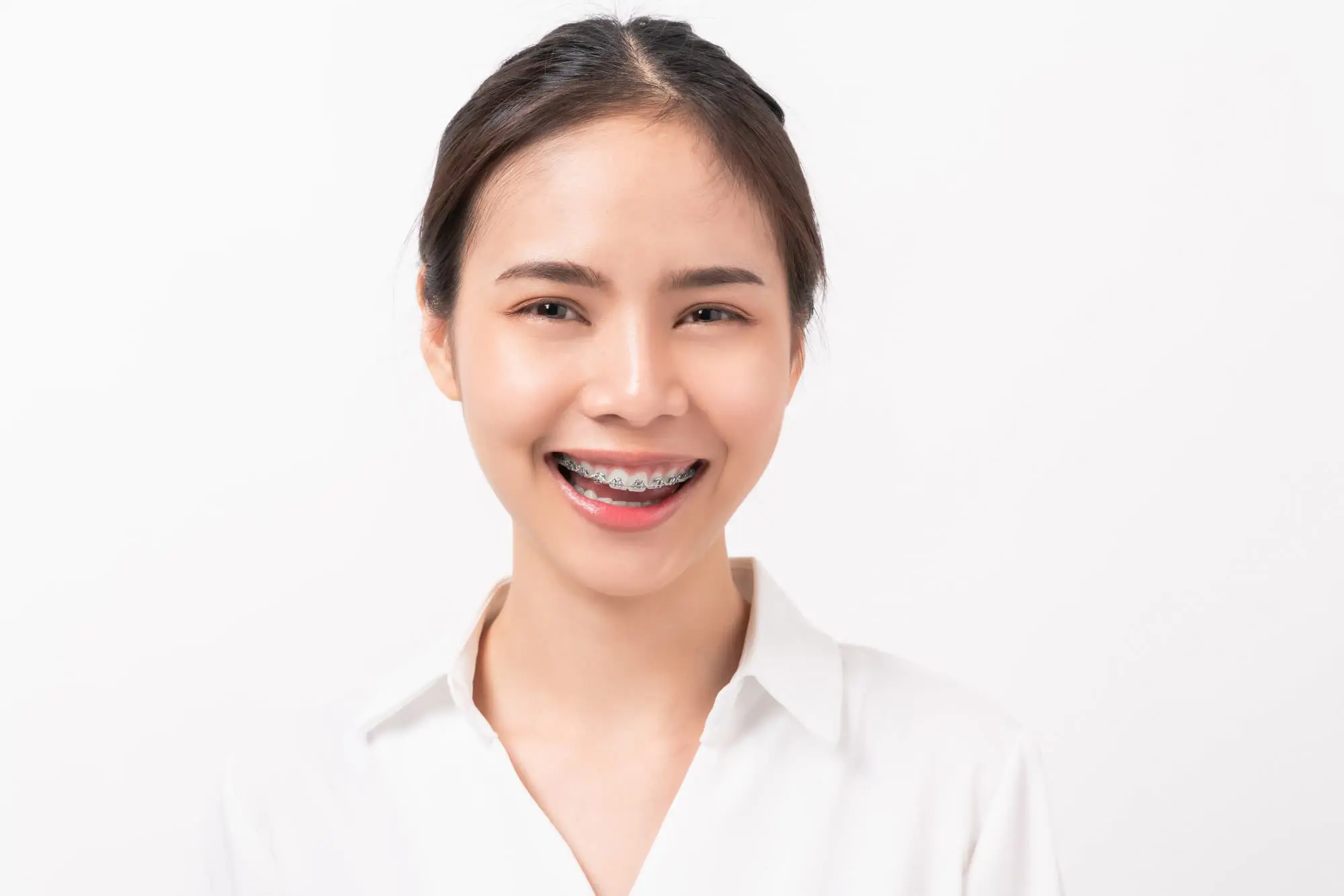 Young woman with dark hair wearing a white shirt, smiling and showing metal braces in Henderson, NV.