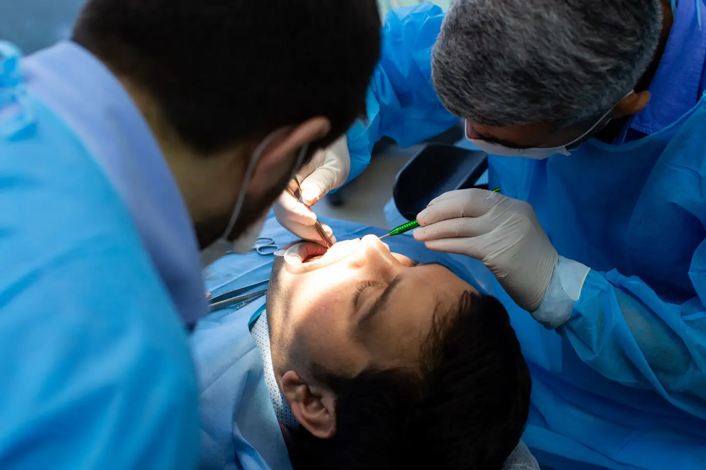 A dentist and assistant, both in blue protective gowns and gloves, examine a patient's mouth for signs of tongue thrust as the patient lies in a dental chair at Chauncey Orthodontics operates in Henderson, NV.