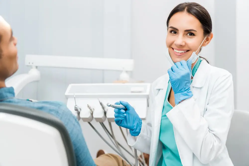 A dentist wearing blue gloves smiles while preparing to treat a patient, ensuring that their orthodontic insurance plans are well understood before sitting in the dental chair in Henderson, NV.