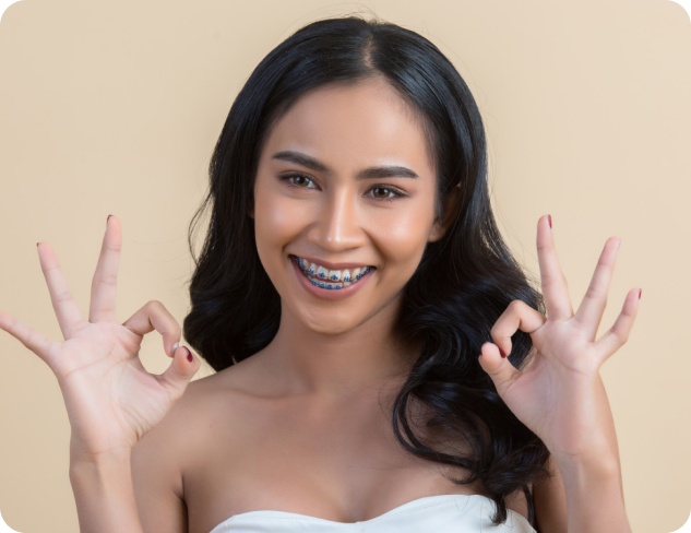 Showcasing the confidence adult orthodontics can bring, a woman with long black hair and braces smiles and makes an "OK" gesture with both hands. Trust Chauncey Orthodontics in Henderson, NV for your smile transformation.
