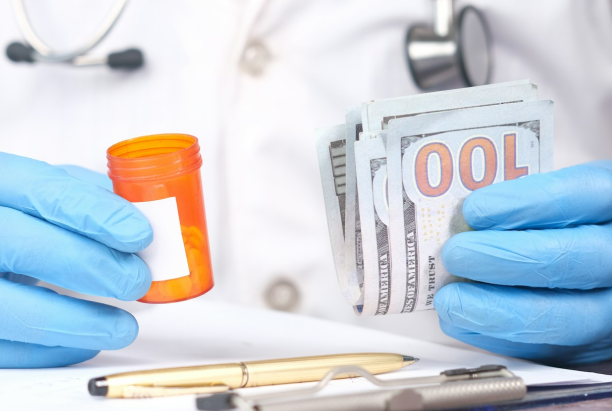 The individual in a lab coat, holding a pill bottle and 100-dollar bills, with blue gloves and a stethoscope visible, might be exploring Invisalign payment options at Chauncey Orthodontics operates in Henderson, NV.