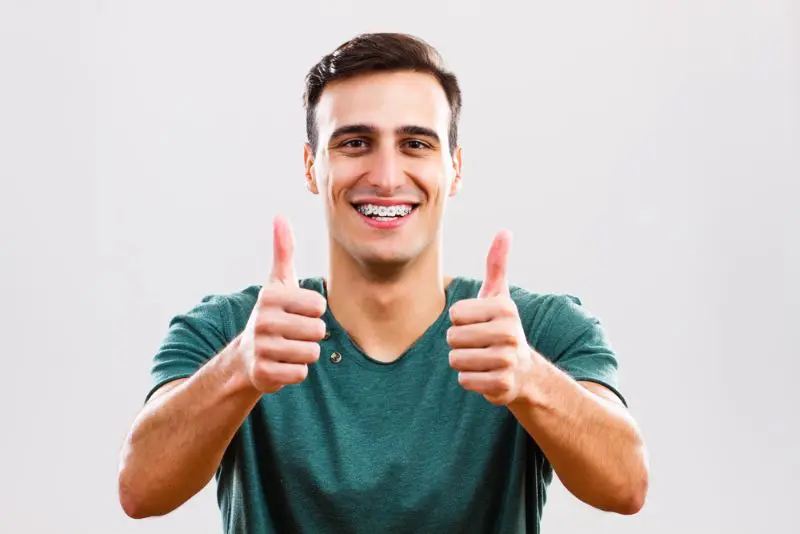 A young man wearing a green shirt and braces smiles and gives two thumbs up cause feel benefit adult brace from Chauncey Orthodontics in Henderson, NV.