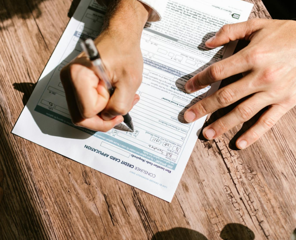 A person is meticulously filling out a invisalign insurance application form with a pen on a wooden surface, Invisalign be covered by insurance at Chauncey Orthodontics operates in Henderson, NV.