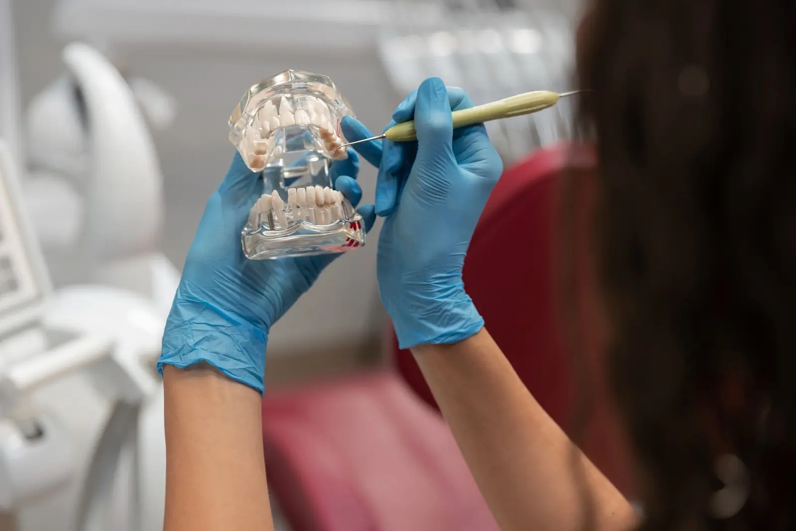 The image shows a person wearing blue gloves holding a dental model and pointing at it with a dental instrument, highlighting the importance of braces and orthodontic insurance in Henderson, NV.