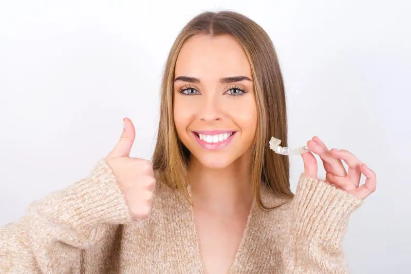 A smiling woman holds a clear dental aligner, contemplating the flexible Invisalign payment plans at Chauncey Orthodontics operates in Henderson, NV.