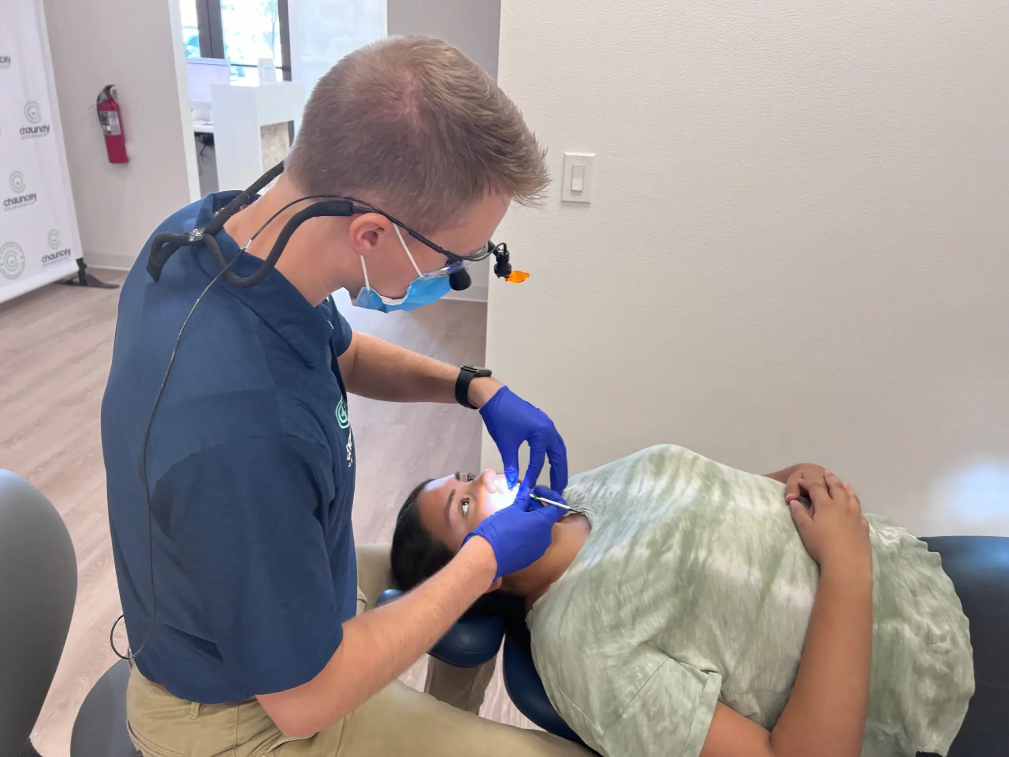 Dr. Tate Chauncey wearing gloves and a mask examines a patient's teeth while the patient lies on a dental chair at Chauncey Orthodontics.