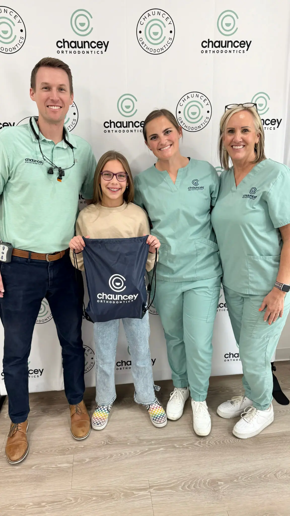 Dr. Tate Chauncey and his team, including a young girl wearing braces in Henderson NV at Chauncey Orthodontics, stand smiling in front of a Chauncey Orthodontics branded backdrop.