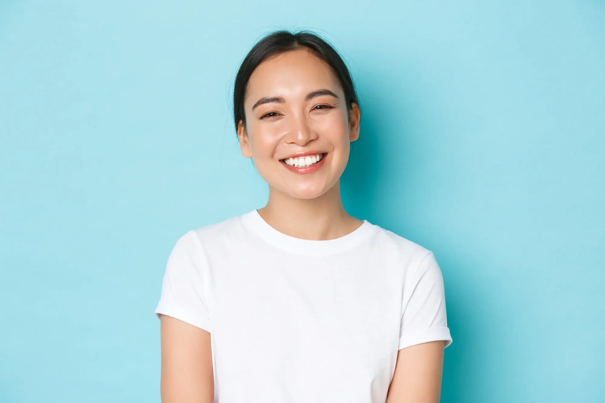 A person in a white t-shirt smiles while standing in front of a plain light blue background at Chauncey Orthodontics in Henderson NV.