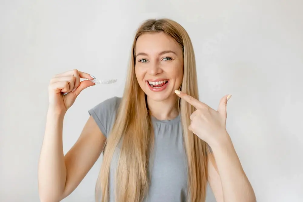 Young woman smiling and holding Invisalign aligner – can Invisalign fix overbite in Henderson, NV.