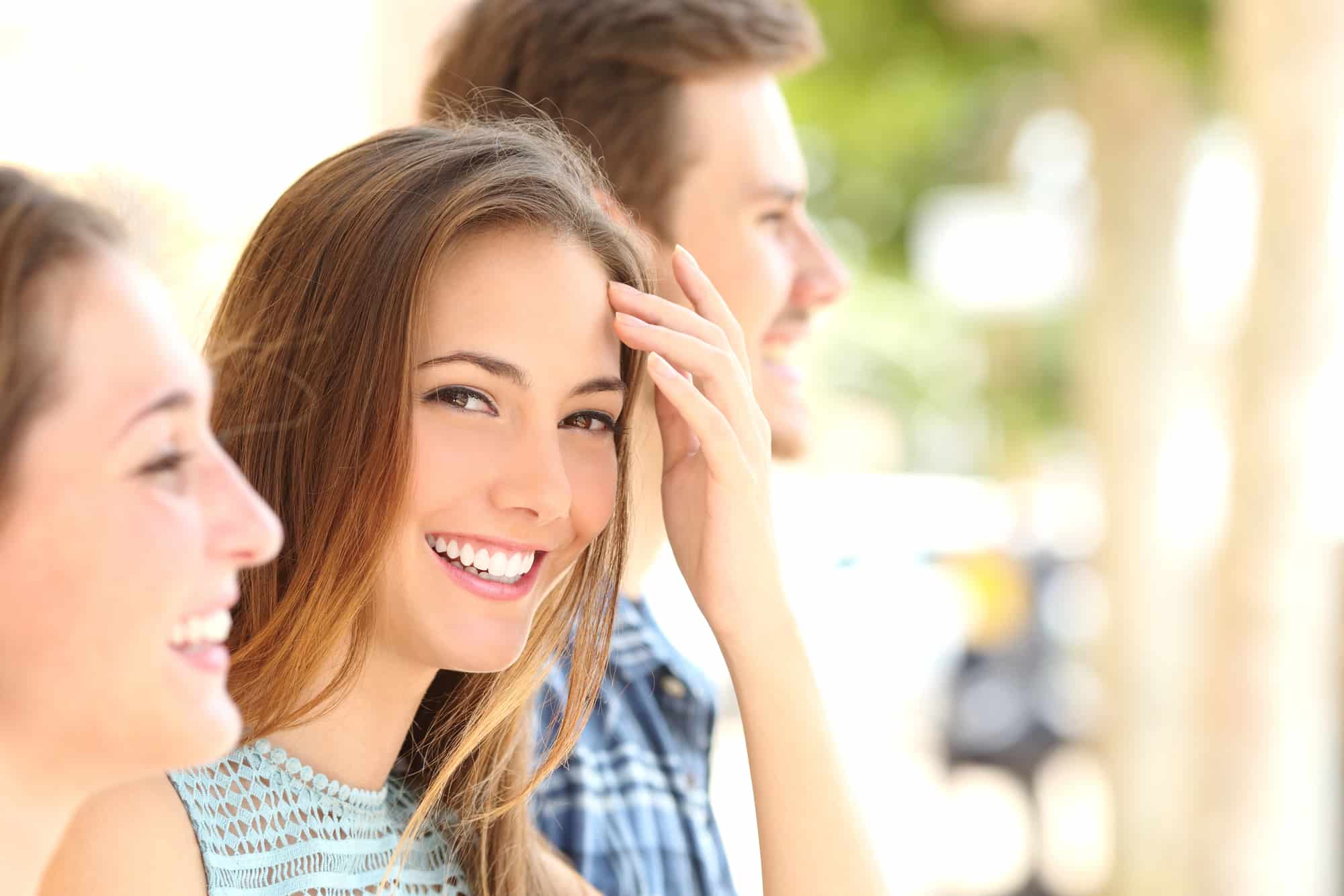Outdoors, three young adults stand in a row the woman in the center smiles, revealing her Herbst Appliance an example of orthodontic care available at Chauncey Orthodontics in Henderson, NV.